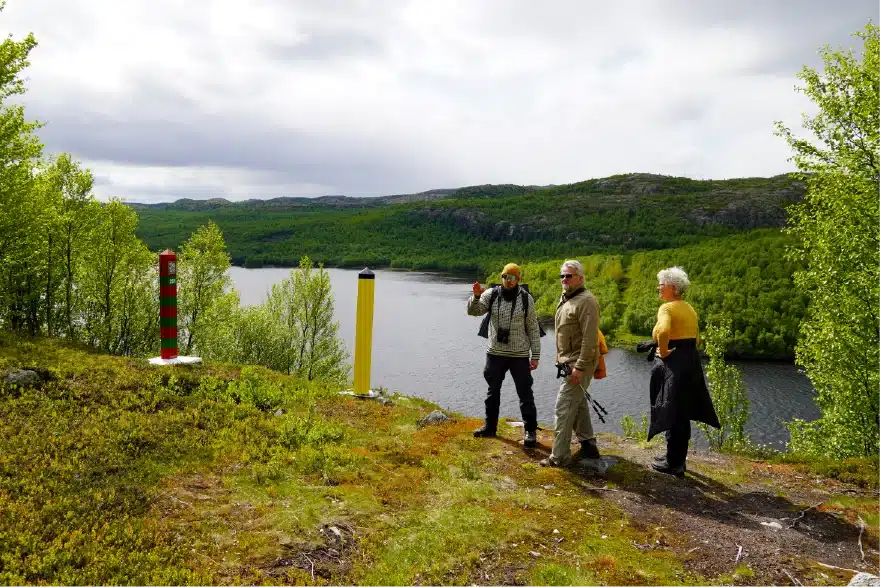 Zwei Gäste mit Reiseführer stehen an den norwegisch-russischen Grenzmarkierungen neben dem Fluss Pasvik