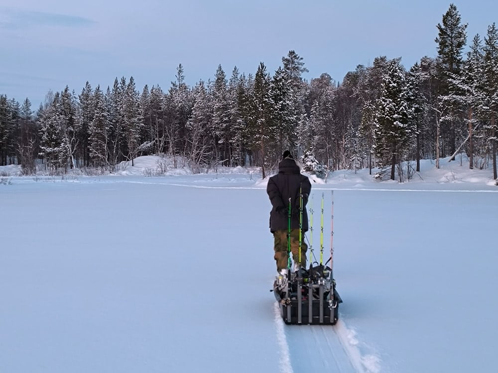 Guide pulling a sled on a frozen lake for ice fishing trip near Kirkenes