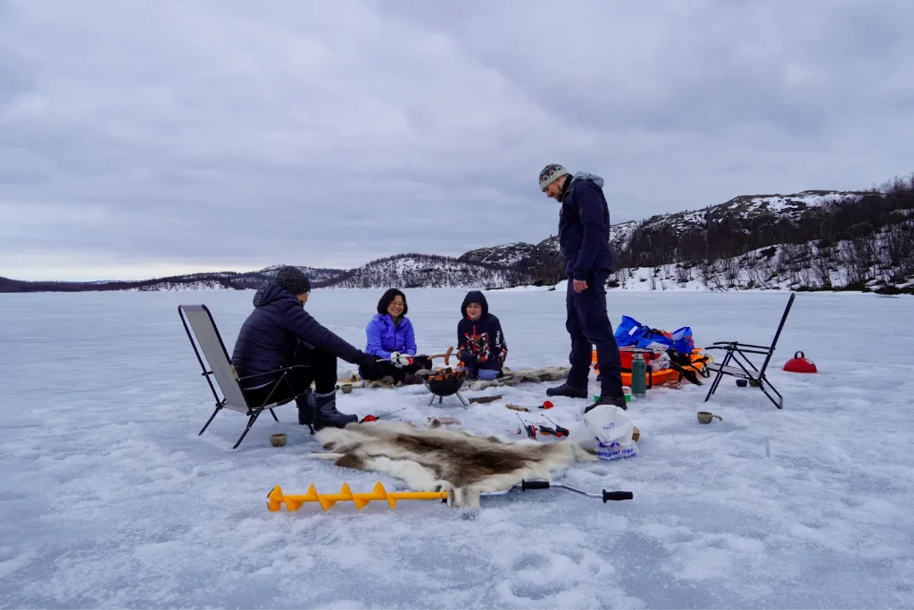 Eisfischen mit der Familie auf einem gefrorenen See in Kirkenes mit Kochen am Lagerfeuer