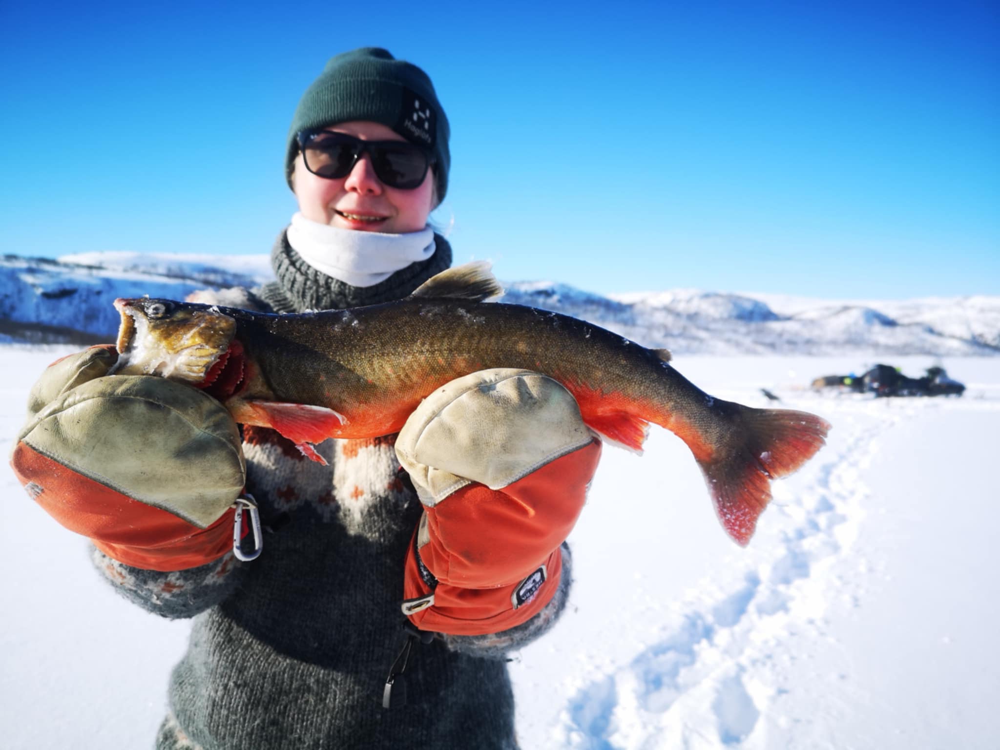 Woman proudly holding fish after a successful ice fishing trip in Kirkenes, Northern Norway