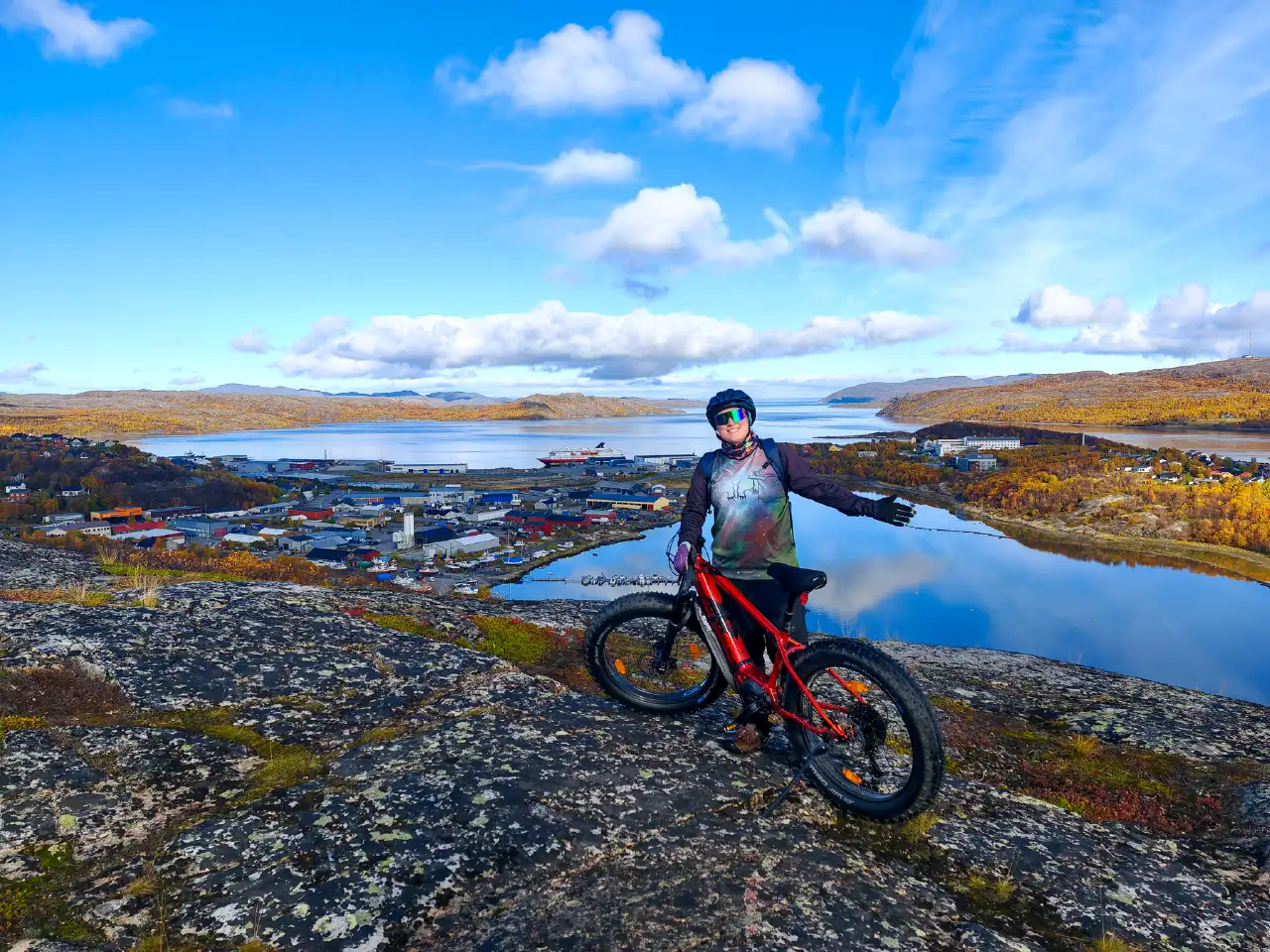 Gast mit einem E-Fatbike mit Blick auf den Hafen von Kirkenes und den Fjord während einer Herrentour in Nordnorwegen.