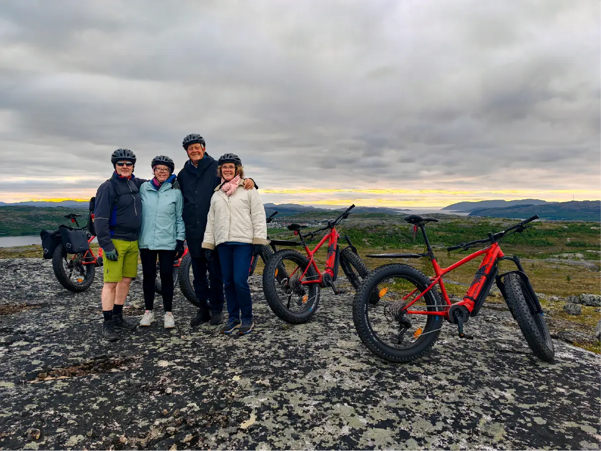 Vier Gäste posieren mit roten E-Fatbikes an einem malerischen Aussichtspunkt mit Blick auf die Fjorde und die arktische Landschaft in der Nähe von Kirkenes während einer geführten E-Fatbike-Tour.
