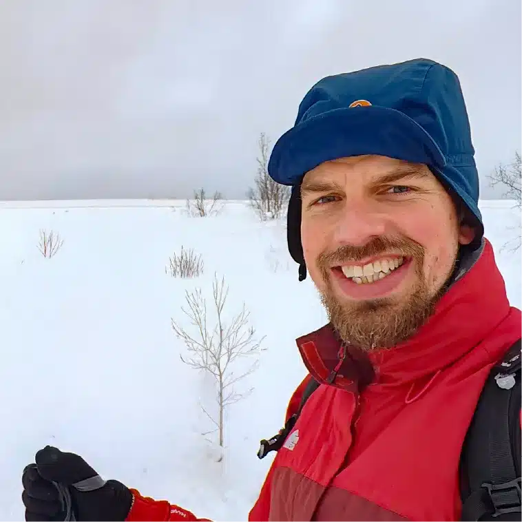 Lächelnde Person mit roter Jacke und Wintermütze bei einer Winterwanderung in der verschneiten Landschaft bei Kirkenes