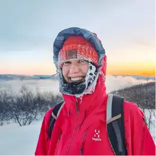 Eine Person lächelt im arktischen Winter mit Frost im Gesicht und trägt eine rote Jacke an einem kalten Tag in der Nähe von Kirkenes