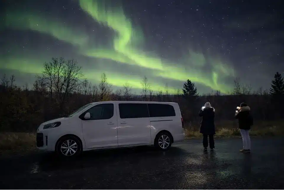 Gäste fotografieren das Nordlicht neben einem Minivan am Straßenrand im Pasvik-Tal bei Kirkenes in Nordnorwegen.