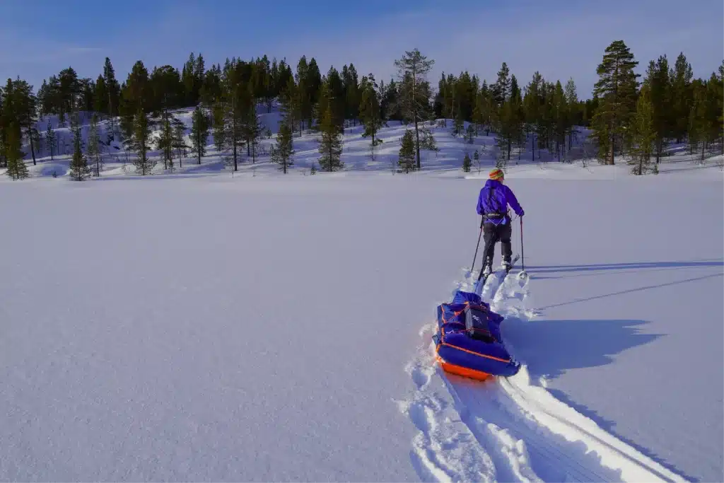 Eine Person, die durch tiefen Schnee Skifahren fährt und einen Pulka-Schlitten zieht, im Pasviktal bei Kirkenes in Nordnorwegen.
