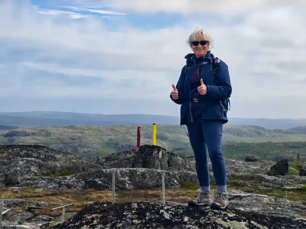 Guest standing on rocky tundra beside the Norway and Russia border markers during the Boris Gleb Russian Border Hike near Kirkenes, Northern Norway.