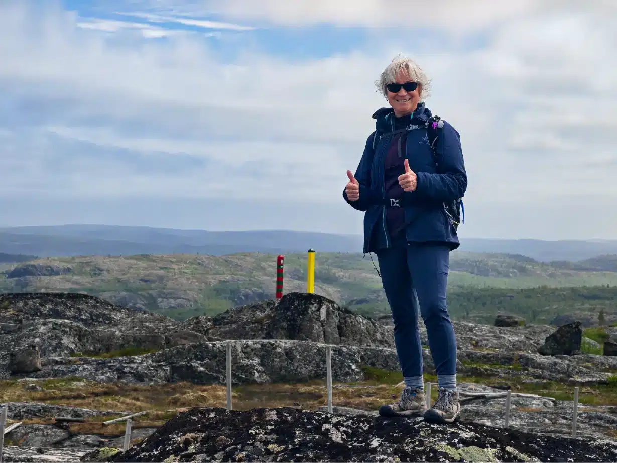 Gast steht auf felsiger Tundra neben den norwegischen und russischen Grenzmarkierungen während der Boris-Gleb-Russland-Grenzwanderung bei Kirkenes, Nordnorwegen.