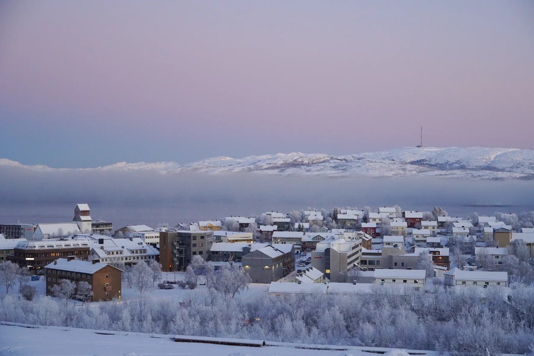 Winterblick über die Stadt Kirkenes mit schneebedeckten Häusern und zugefrorenem Fjord bei Sonnenuntergang im Dezember