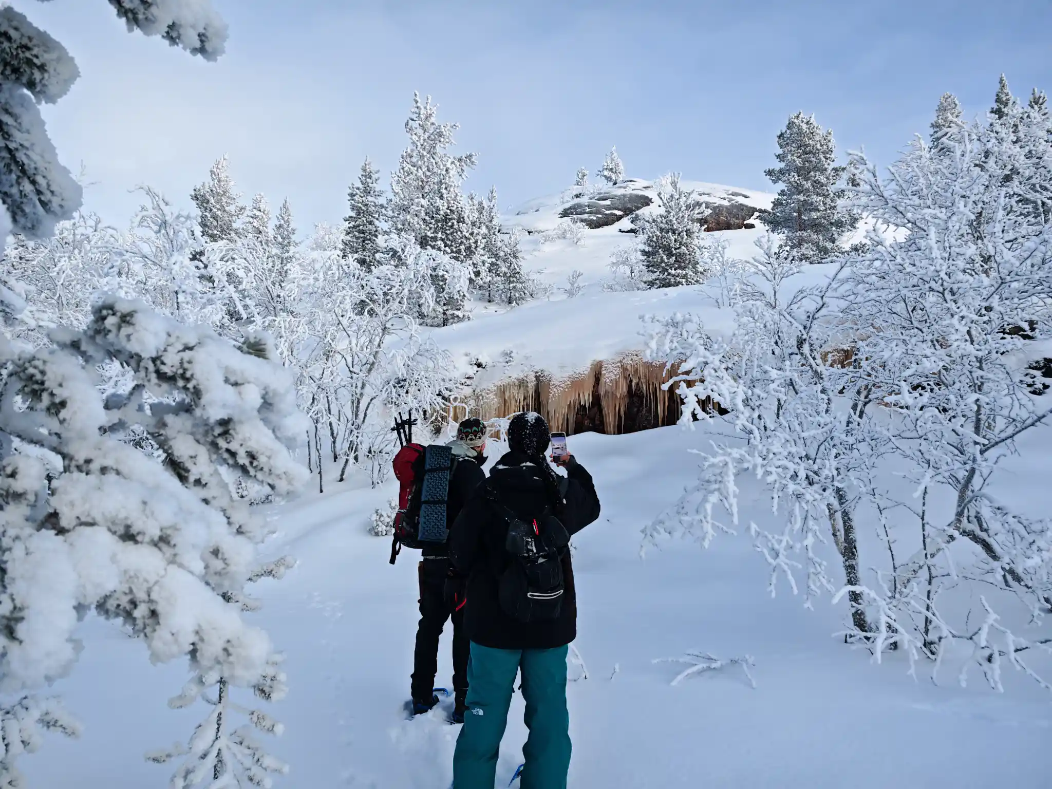 Zwei Leute wandern mit Schneeschuhen durch einen verschneiten Wald und halten an, um gefrorene Eiszapfen nahe der norwegisch-russischen Grenze bei Kirkenes in Nordnorwegen zu fotografieren.