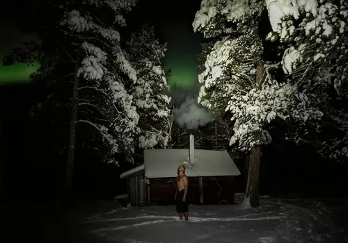 Man enjoying an Arctic wilderness sauna at Namdalen under the Northern Lights near Kirkenes, Northern Norway