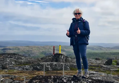 Guest standing on rocky tundra beside the Norway and Russia border markers during the Boris Gleb Russian Border Hike near Kirkenes, Northern Norway.