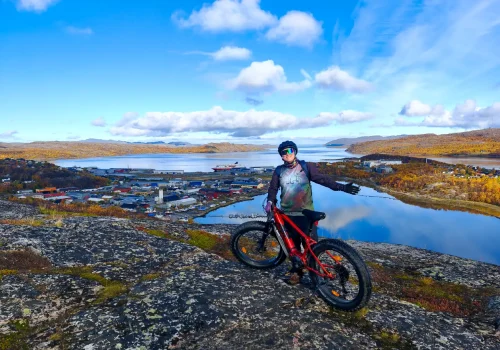 Guest with an e-fatbike overlooking Kirkenes habour and the fjord during an autumn tour in Northern Norway.