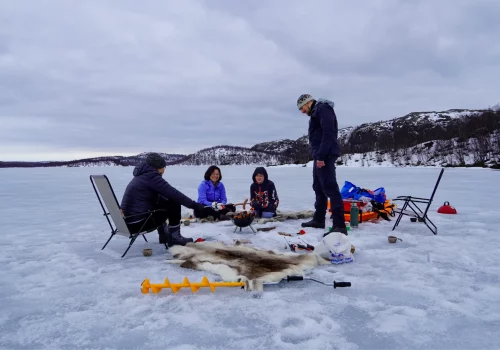 Eisfischen mit der Familie auf einem gefrorenen See in Kirkenes mit Kochen am Lagerfeuer