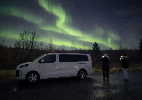 Guests photographing the Northern Lights next to a minivan on a roadside in the Pasvik Valley near Kirkenes in Northern Norway.