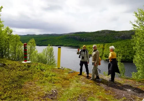 Zwei Gäste mit Reiseführer stehen an den norwegisch-russischen Grenzmarkierungen neben dem Fluss Pasvik