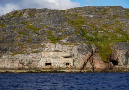 Blick vom Boot auf eine Torpedobatterie aus dem Zweiten Weltkrieg bei Kirkenes in Nordnorwegen