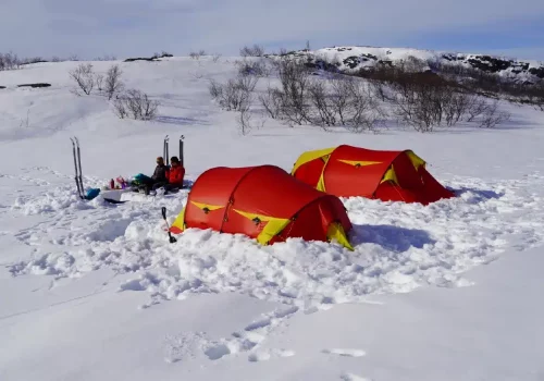 Winter Expeditionslager mit zwei Zelten und Menschen, die in Kirkenes in Nordnorwegen im Schnee kochen.